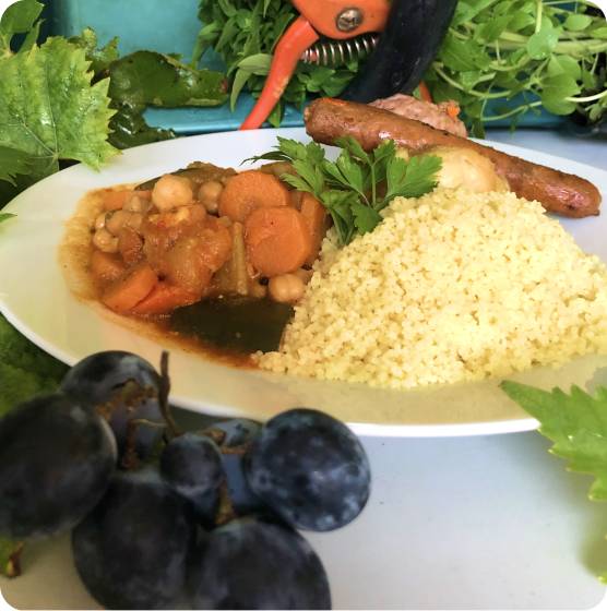 Assiette de couscous garnie de ragoût de pois chiches et carottes, merguez et raisins noirs